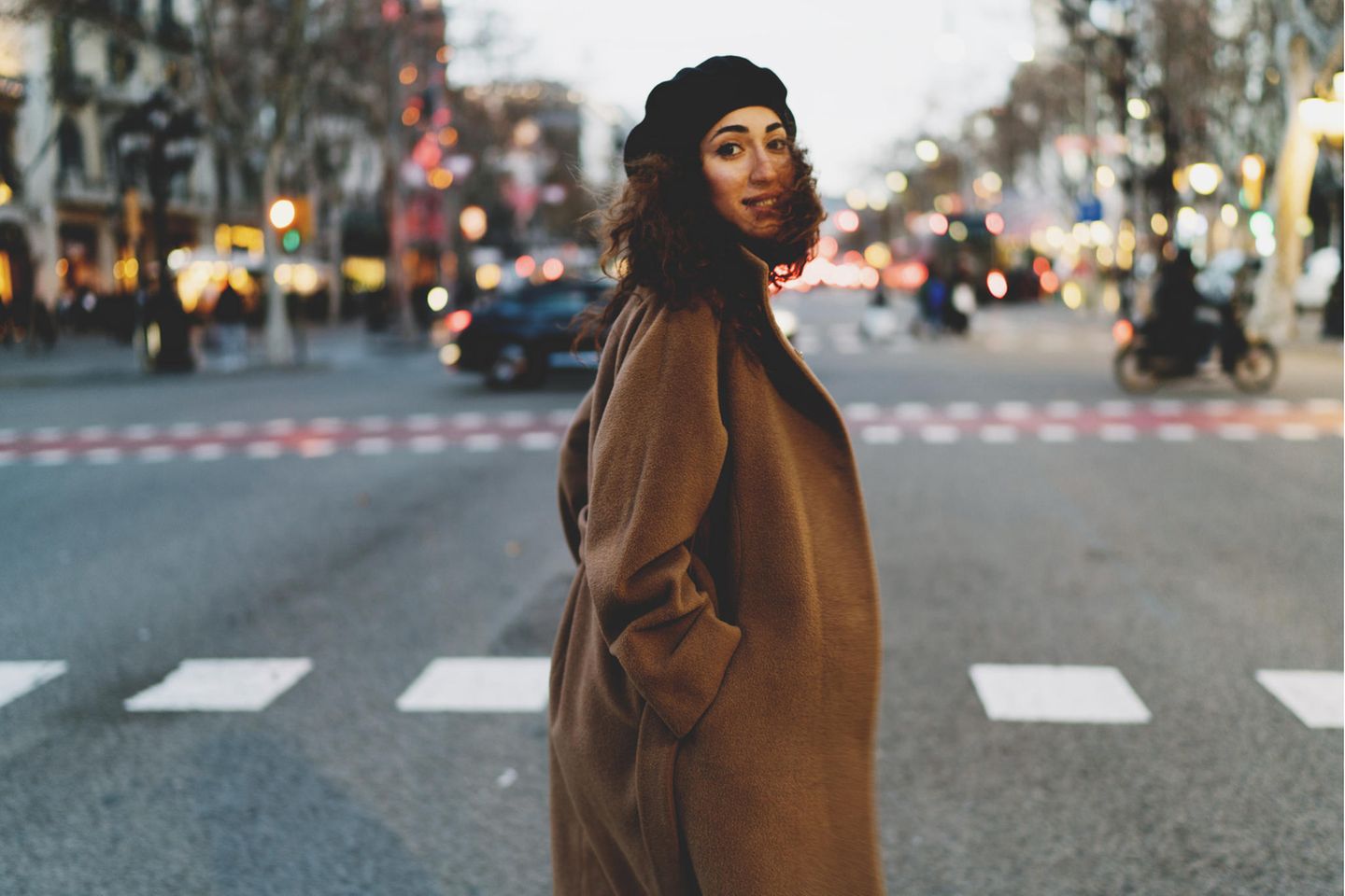 Frau steht auf einer großen Straße und trägt einen braunen Wintermantel