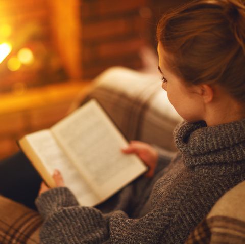 Frau liest vor dem Kamin ein Buch: Diese 5 düsteren Romane sind die perfekte Herbstlektüre