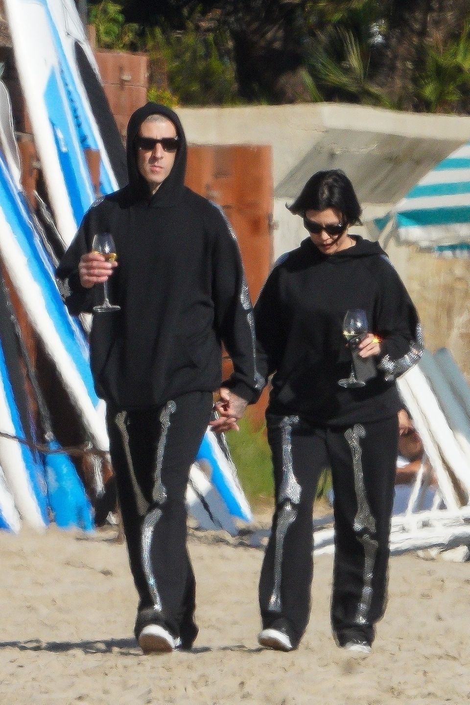 Kourtney Kardashian und Travis Barker feiern das einjährige Jubiläum ihrer Verlobung ganz gemütlich mit zwei Gläsern Wein am Strand von Santa Barbara. Die Outfits der Wahl? Schwarze Jogging-Anzüge mit Gruselfaktor. So blitzen Skelettknochen an den Ärmelseiten der Hoodies und an den Frontseiten der Hosen auf. Ganz schön schaurig!