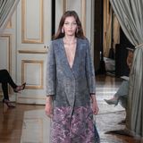 Auf dem Runway bei der Präsentation der Herbst- / Winterkollektion 2021/22 wird der Mantel von Armani Privé zum stylischen Hingucker, wirkt jedoch ohne Abwandlung nach royalem Protokoll noch einmal deutlich moderner. Statt hochgeschlossenem Saum besticht der Midi-Coat mit tiefem Ausschnitt und schimmerndem Stoff. In Kombination mit weiter Satinhose und Babuschen im gleichen Stoff bekommt das Laufsteg-Outfit einen lässigeren Touch.