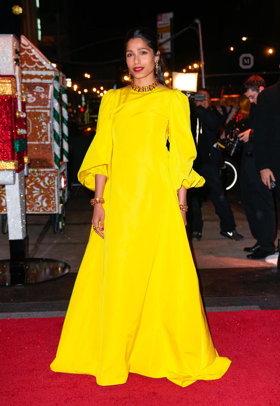 Schauspielerin Freida Pinto setzt auf Knallfarbe! In einem kanariengelben Kleid in A-Linie und mit Puffärmeln, strahlt sie auf dem roten Teppich. Den Look betont sie nur noch mit goldenen Accessoires.