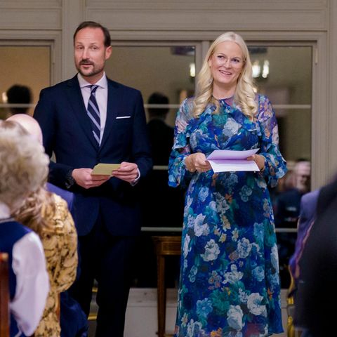 In diesem floralen Kleid begrüßt Kronprinzessin Mette-Marit von Norwegen zusammen mit ihrem Ehemann Kronprinz Haakon Gäste auf Gut Skaugum bei Oslo. Das mittellange Kleid in Blautönen ist von dem australischen Label Zimmermann. Dazu trägt sie beige Pumps und eine gold gerahmte Brille von Dior. Prinz Haakon wählt passend zu Mette-Marits Kleid, einen dunkelblauen Anzug mit Krawatte.