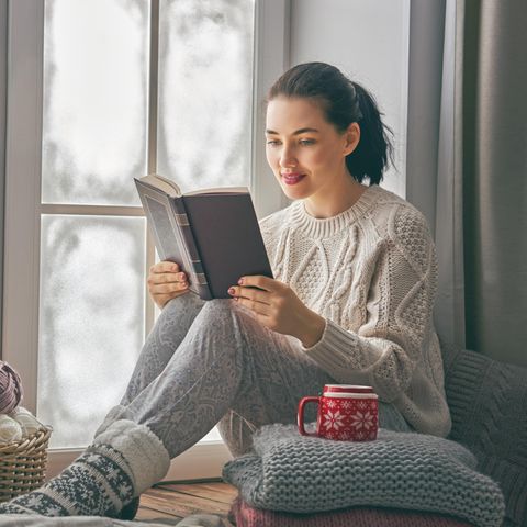 Frau mit Buch am Fenster im Winter