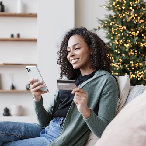 Frau mit Kreditkarte beim Online-Shopping vor Weihnachtsbaum