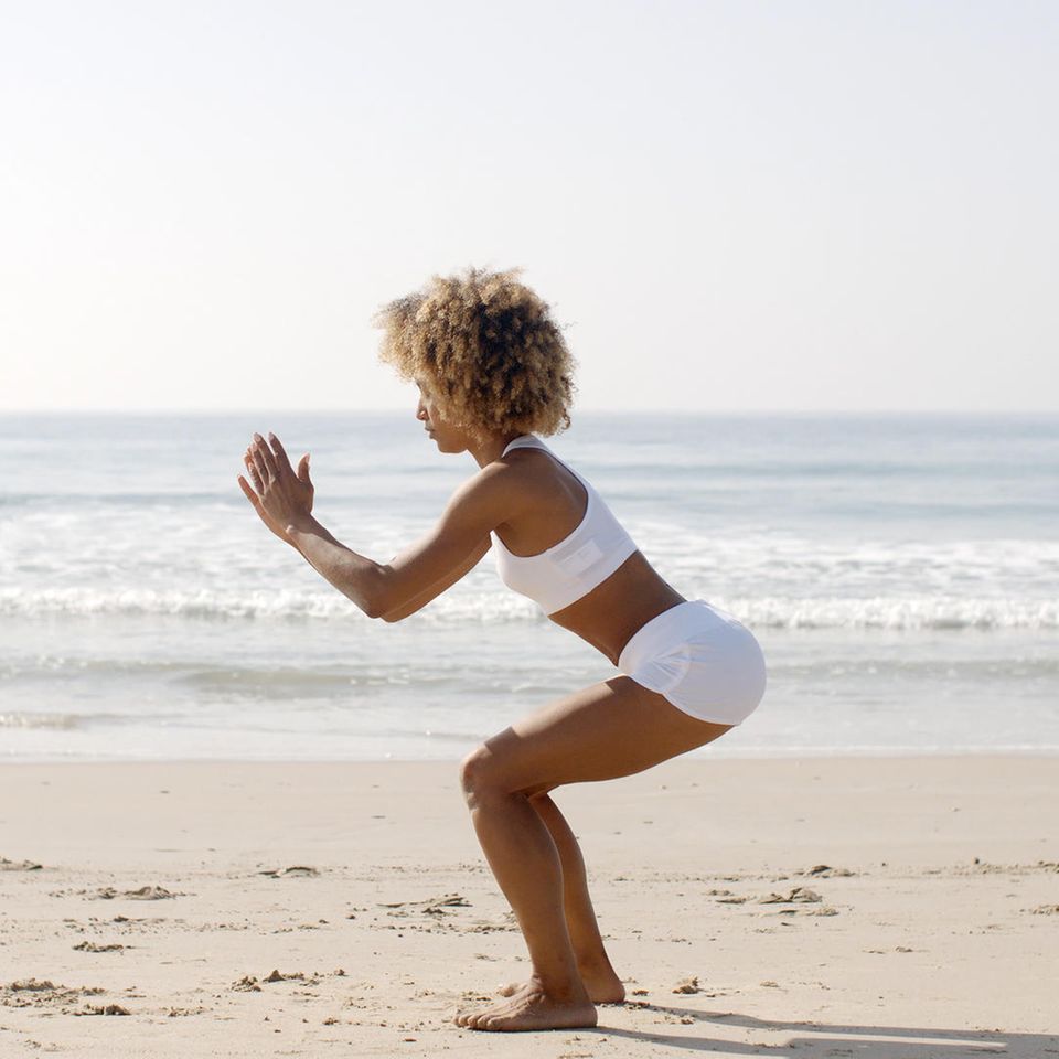 Frau am Strand im Squat: Das passiert im Körper, wenn Sie täglich Squats machen