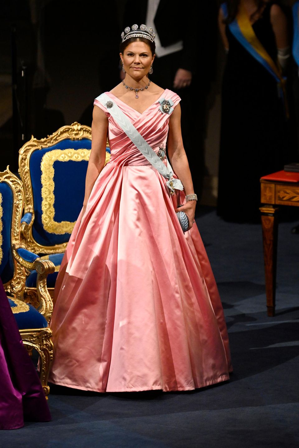 Prinzessin Victoria zeigt sich hingegen mit rosafarbener Seide in einem zarten Rosa und gesteppter Clutch in Babyblau.