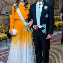 Ungewöhnlich, aber ein echter Hingucker ist Prinzessin Sofias Seidenkleid von Lilli Jahilo mit orangegelb-weißem Farbverlauf, dazu trägt sie eine weiße Clutch mit Flechtoptik von Bottega Veneta. So führt Prinz Carl Philip seine schöne Frau natürlich besonders gerne in den Festsaal des Königschlosses in Stockholm.