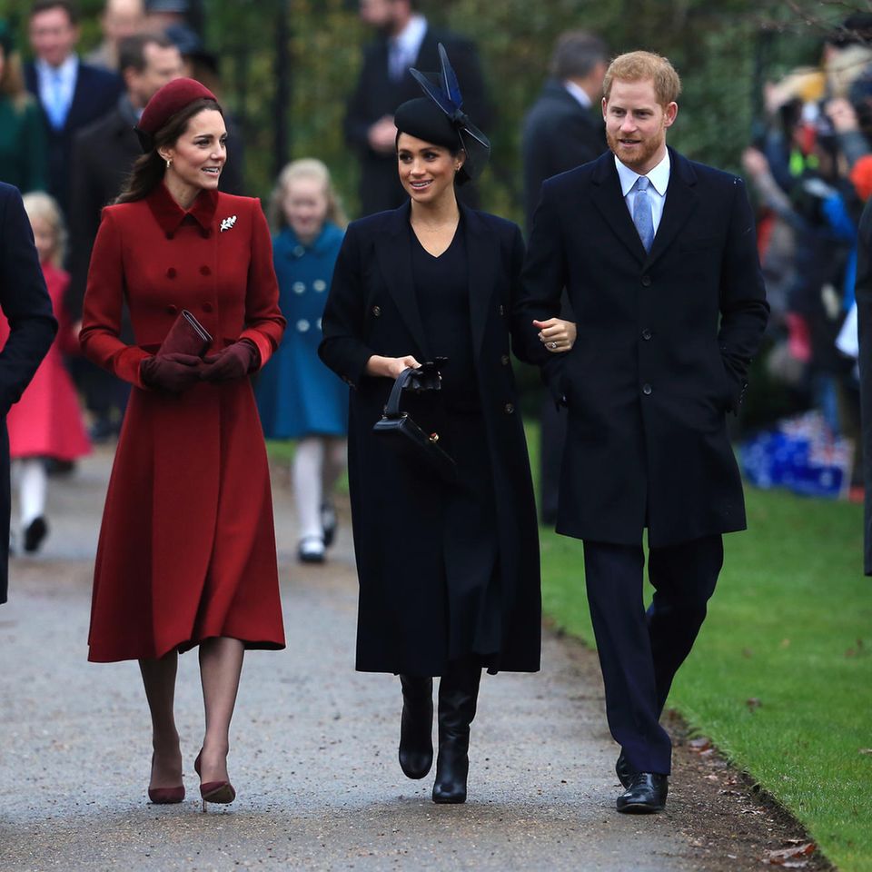 Meghans erstes Weihnachtsfest als Herzogin von Sussex. In einem dunkelblauen Mantel sticht sie neben Kate in Weinrot und neben Harry und William in Dunkelblau nicht hervor. 