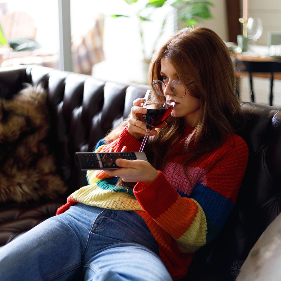 Frau trinkt Wein auf der Couch: Durch diese Alltagsfehler nehmen Sie zu – ohne es zu merken