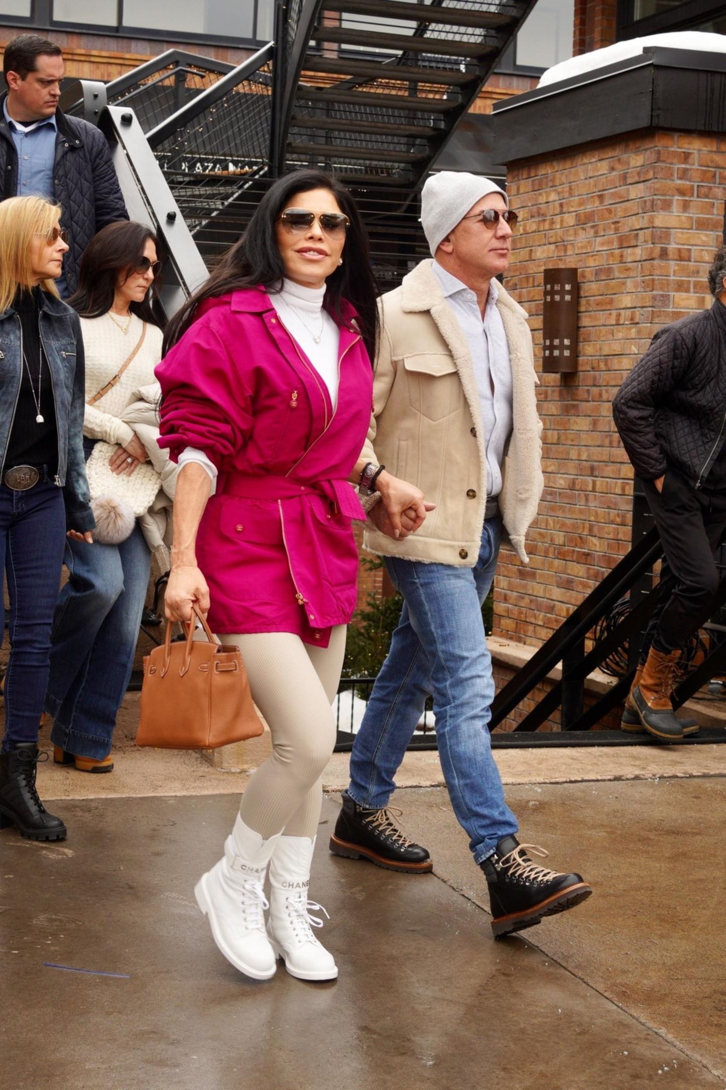 Händchenhaltend spazieren Jeff Bezos und seine Freundin Lauren Sanchez für einen Einkaufsbummel durch Aspen, Colorado. In cremefarbener Jacke, Jeans und mit schlichter Strickmütze sieht der Amazon-Milliardär stylisch, aber dennoch bodenständig aus. Neben ihm setzt Lauren Sanchez auf einen Farbakzent: Zu ihren weißen Chanel-Schnürschuhen ist die pinkfarbene Jacke mit Taillenbindung definitiv ein Hingucker. 
