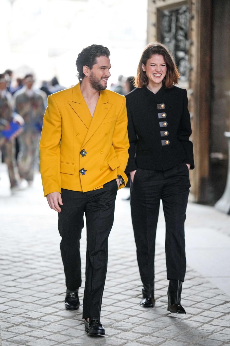 Für die Modenschau von Louis Vuitton sind Kit Harington und Rose Leslie in der Stadt der Liebe – und das sieht man den beiden direkt an. Er wirft ihr einen verliebten Blick zu, sie strahlt. Während Leslie auf ein lässiges Ensemble in Schwarz setzt, begeistert Kit in strahlendem Gelb. Natürlich sind beide Looks von Louis Vuitton.