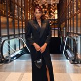 Influencerin und Model Didi Stone posiert im schwarzen langen Blazerkleid und ergänzt ihr schickes Outfit um die Boîte Love Clutch von Saint Laurent und silbernen Schmuck.