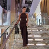 Im langen braunen Kleid schreitet Sängerin und Autorin Mandy Capristo die Treppen in dem neuen Luxushotel hinab. Zum klassischen Make-up in Brauntönen kombiniert sie ebenfalls einen brauen Shopper zum schlichten Kleid.