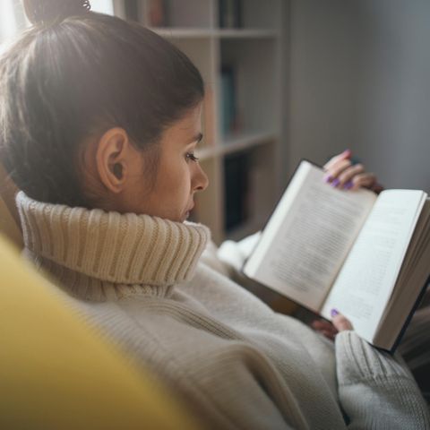 Frau liest im Sessel: Diese 5 Bücher sind perfekt, um dem Winterblues zu entkommen