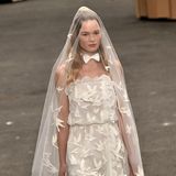Model Anna Ewers präsentiert einen Wedding-inspirierten Look aus kurzem Kleid mit weißen Tauben und passendem Schleier. Eine weiße Fliege rundet das Thema ab. 