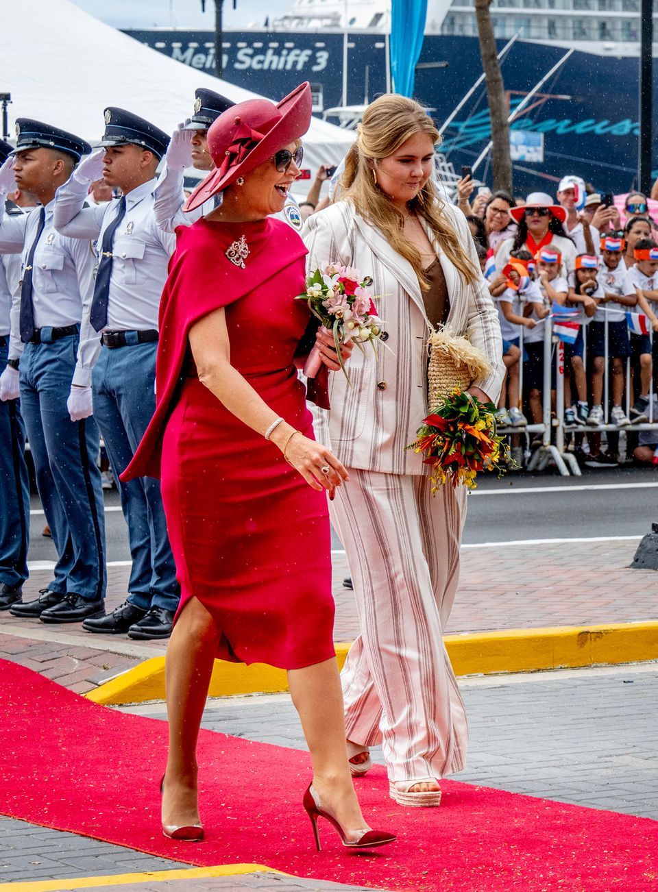 Tag 4  Die niederländische Königsfamilie ist auf Aruba angekommen! Königin Máxima glänzt in einem feuerroten Cape-Kleid und passendem Hut mit XL-Krempe, Prinzessin Amalia besticht in einem gestreiften Hosenanzug.
