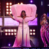 Lizzo ist bekannt dafür, dass ihre Outfits immer etwas extra sind. Auch bei den Brit Awards fällt sie auf. In einem Look aus rosafarbenem Seidenrock, transparenter Korsage und einem nach oben stehenden Cape aus rosafarbenem Tüll betritt sie die Bühne.