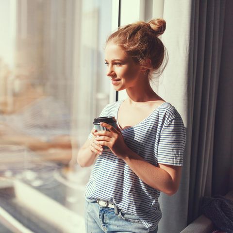 Lächelnde Frau am Fenster: 5 Gewohnheiten glücklicher Menschen