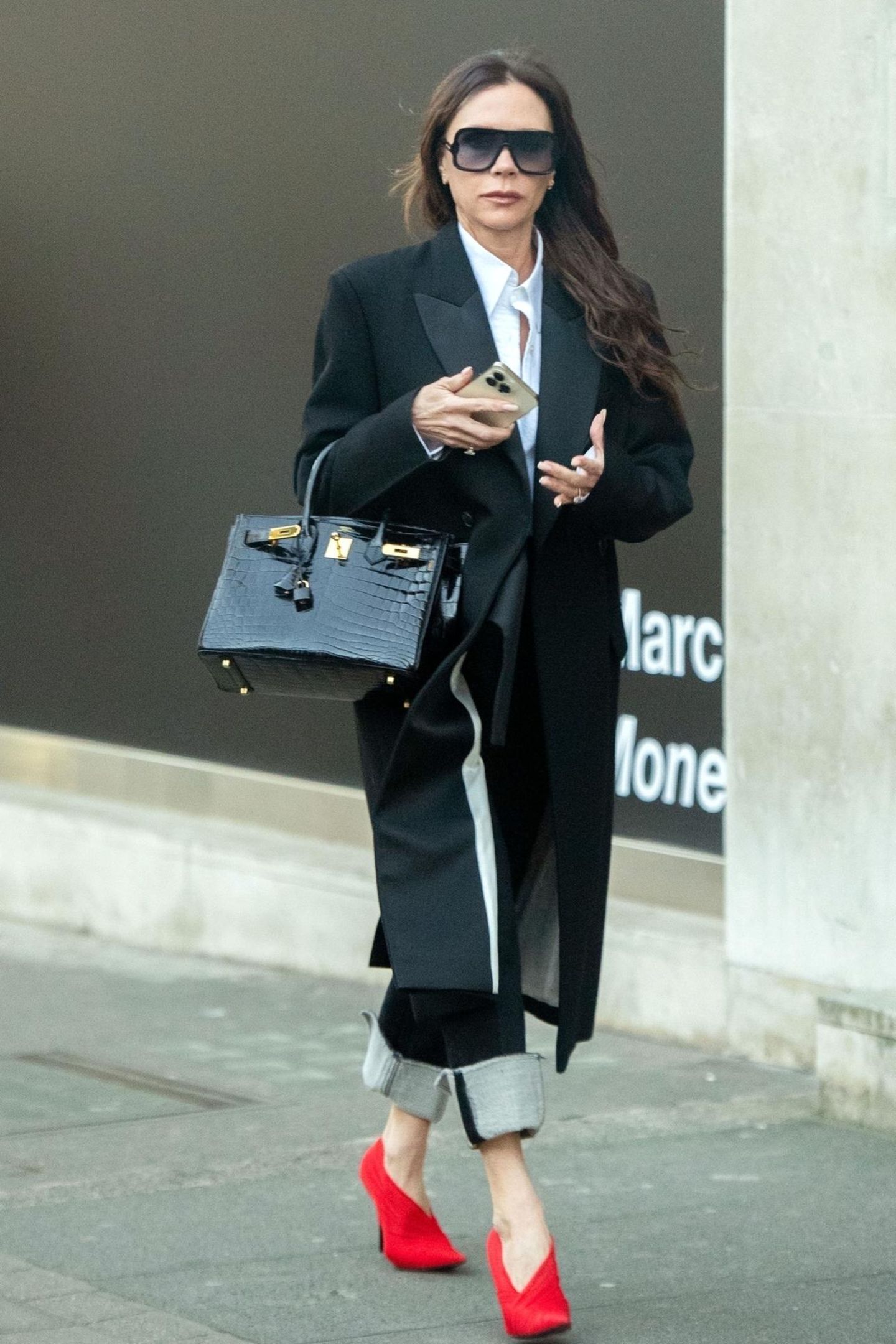 Victoria Beckham bleibt mit diesem Look in ihrer gewohnten Farbfamilie und setzt auf Wollmantel und weißes Hemd. Knallrote Heels mit graphischem Absatz verleihen dem Look der Designerin eine edgy, aber dennoch sexy Komponente.