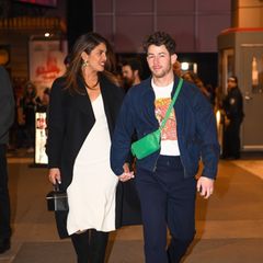 Die Jonas Brothers und ihre Ehefrauen zeigen sich gewohnt stylisch: Priyanka Chopra trägt ein weißes Kleid mit schwarzem Mantel und schwarzen Accessoires. Nick Jonas hat sich für einen coolen Jeans-Look entschieden und trägt zur Jeansjacke eine grüne Umhängetasche und ein Comic-Shirt. 
