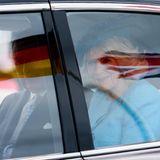Die Flaggen spiegeln sich in der Scheibe des Autos wieder. Charles und Camilla lächeln den Fotografen bei der Abfahrt zu. 