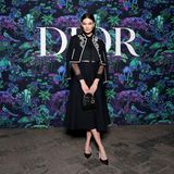 Karlie Kloss nimmt in einem eleganten schwarzen Outfit an der Dior-Show teil. Das Model trägt eine kurze schwarze Jacke mit weißer Stickerei. Dies und die weißen Schleifen an ihren Dior Pumps sind die einzigen Farbakzente des edlen Looks. Besonders niedlich ist die kleine Lady Dior Bag in Lack-Optik.