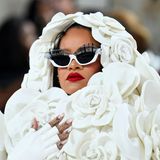 Falsche Wimpern in Übergröße zieren die weiße Statement-Sonnenbrille von Rihanna. Ihre besondere Lippenform mit dem ausgeprägten Lippenherz schminkt die Sängerin in einem tiefen Rotton, der ihren weißen Look aufbricht. 