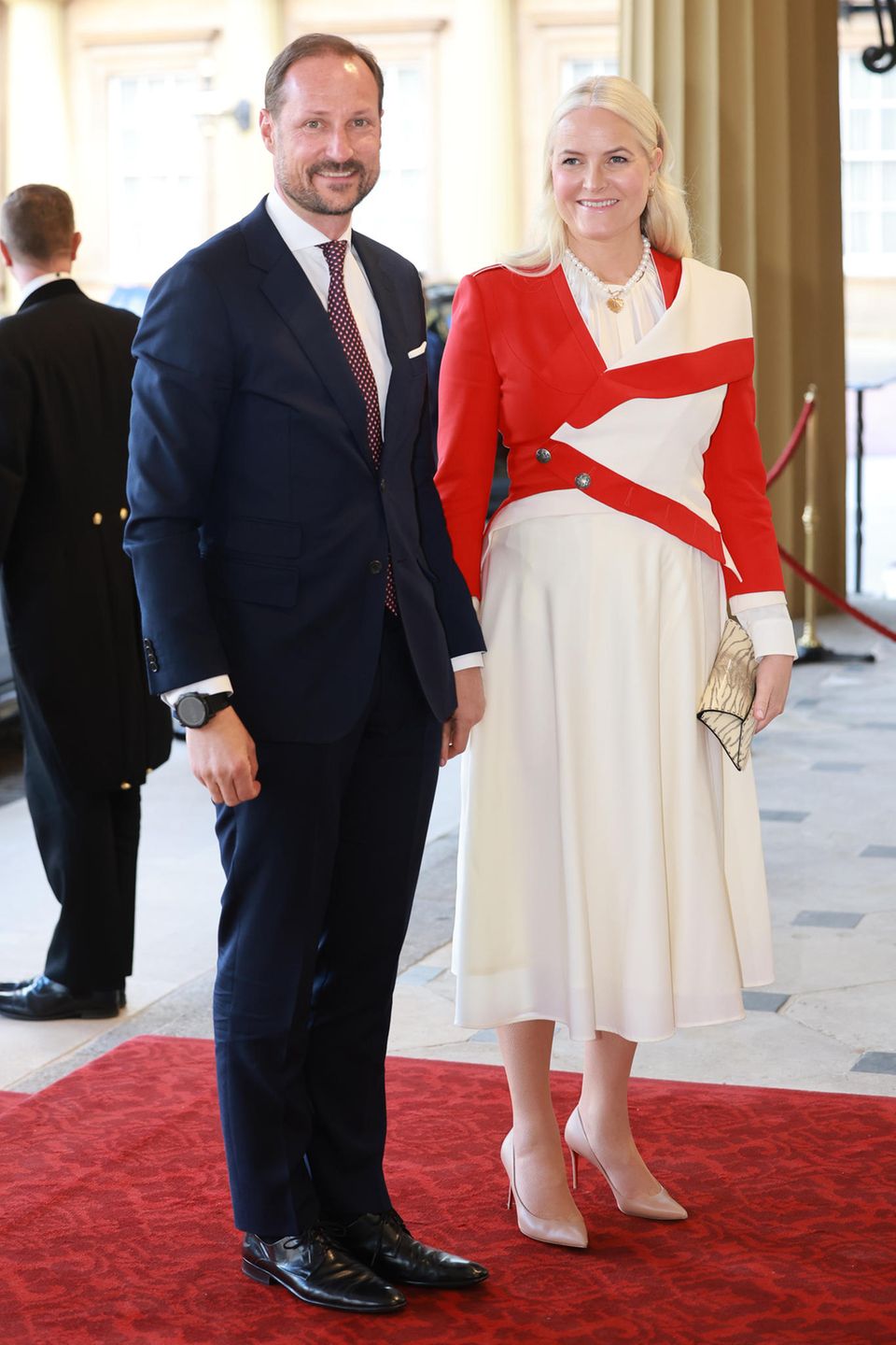 Prinzessin Mette-Marit verzaubert neben ihrem Mann Prinz Haakon in einem cremefarbenen Kleid mit leuchtend rotem Jäckchen.