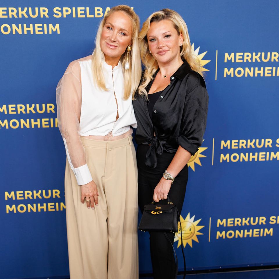 Im perfekten modischen Kontrastprogramm zeigen sich Janine Kunze und Evelyn Burdecki bei der großen Eröffnung der Merkur Spielbank in Monheim. Während Janine zur beigen Stoffhose, einer semitransparenten Bluse und altrosafarbenen Pumps greift, präferiert Evelyn Schwarz und stylt zur dunklen Schlitzhose eine glänzende schwarze Bluse sowie keine Mini-Kelly-Bag von Hermes. 