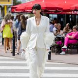 Farblich schlicht und dennoch mit Wow-Effekt: Model Katya Tolstova stylt zum weißen Anzug mit Federdetails, glitzende Pumps und Mini-Bag. Rote Lippen zum dunklen Haar bringen zusätzlichen Glamour. 