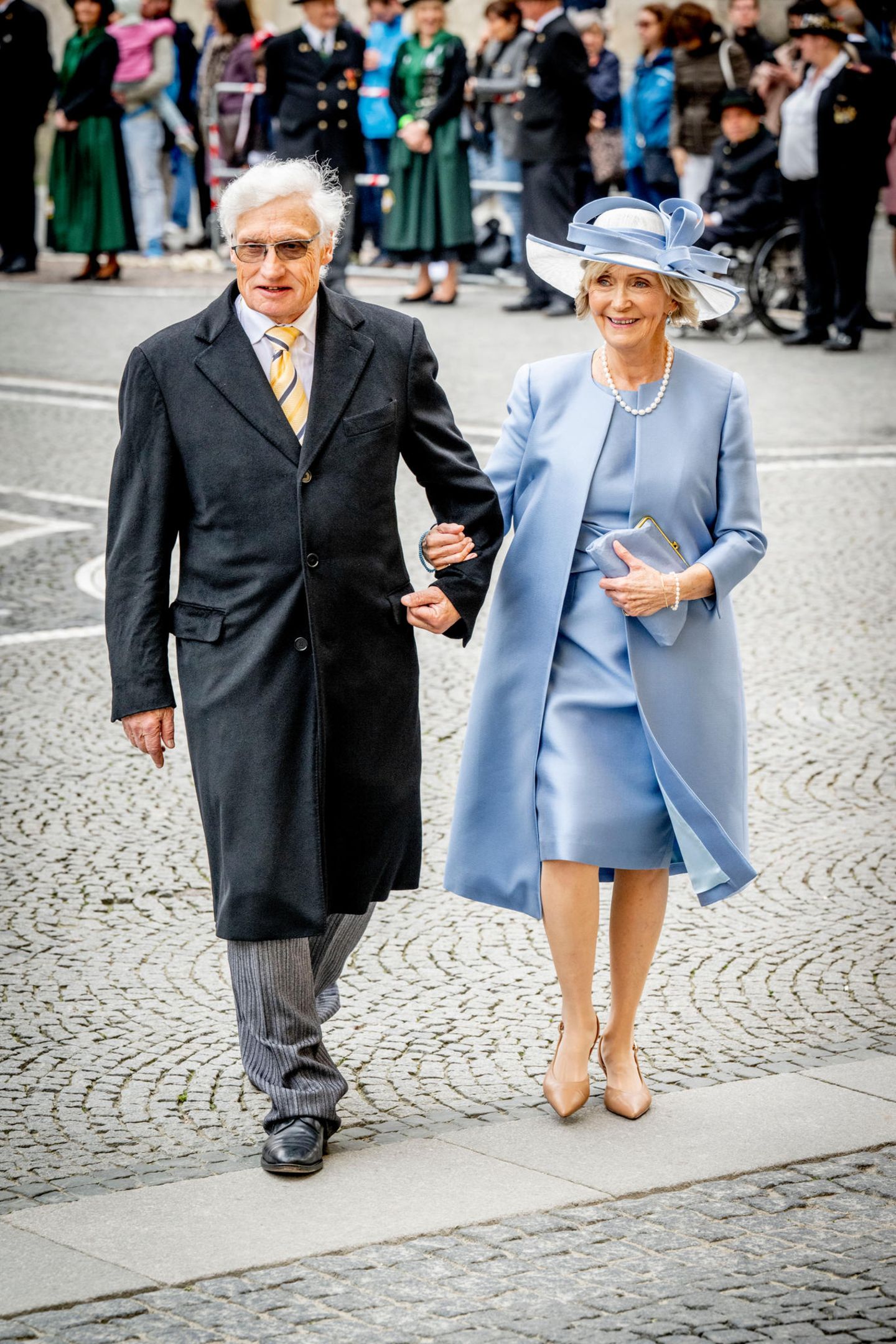 Prinz Luitpold von Bayern erscheint mit der Mutter der Braut, Veronica Taylor, zur Trauung von Ludwig, Prinz von Bayern, und Sophie-Alexandra Evekink. Die Brautmutter begeistert in einem hellblauen Satinkleid mit passendem Hut und Mantel. 