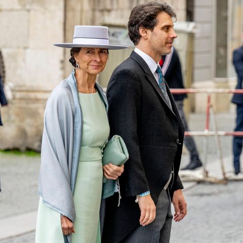 Ludwig, Prinz von Bayern, wird von seiner Mutter Katrin Beatrix Wiegand zur Kirche begleitet. Die Mutter des Bräutigams setzt an diesem wichtigen Tag auf einen zeitlosen und eleganten Look. Zum Etuikleid kombiniert sie einen grauen Hut mit farblich passendem Schultertuch – dezent, aber klassisch. 