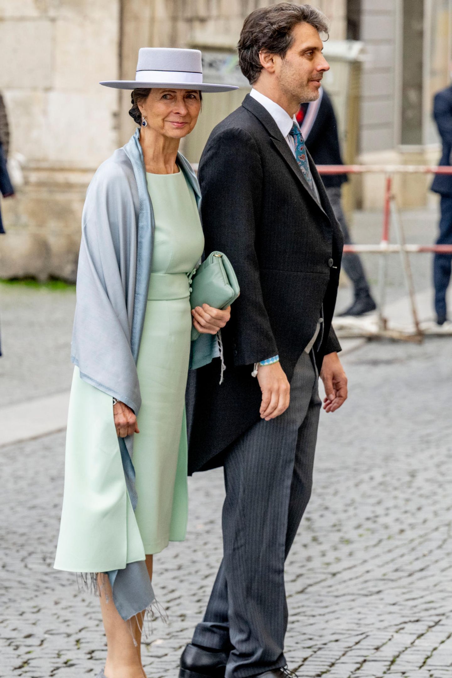 Ludwig, Prinz von Bayern, wird von seiner Mutter Katrin Beatrix Wiegand zur Kirche begleitet. Die Mutter des Bräutigams setzt an diesem wichtigen Tag auf einen zeitlosen und eleganten Look. Zum Etuikleid kombiniert sie einen grauen Hut mit farblich passendem Schultertuch – dezent, aber klassisch. 