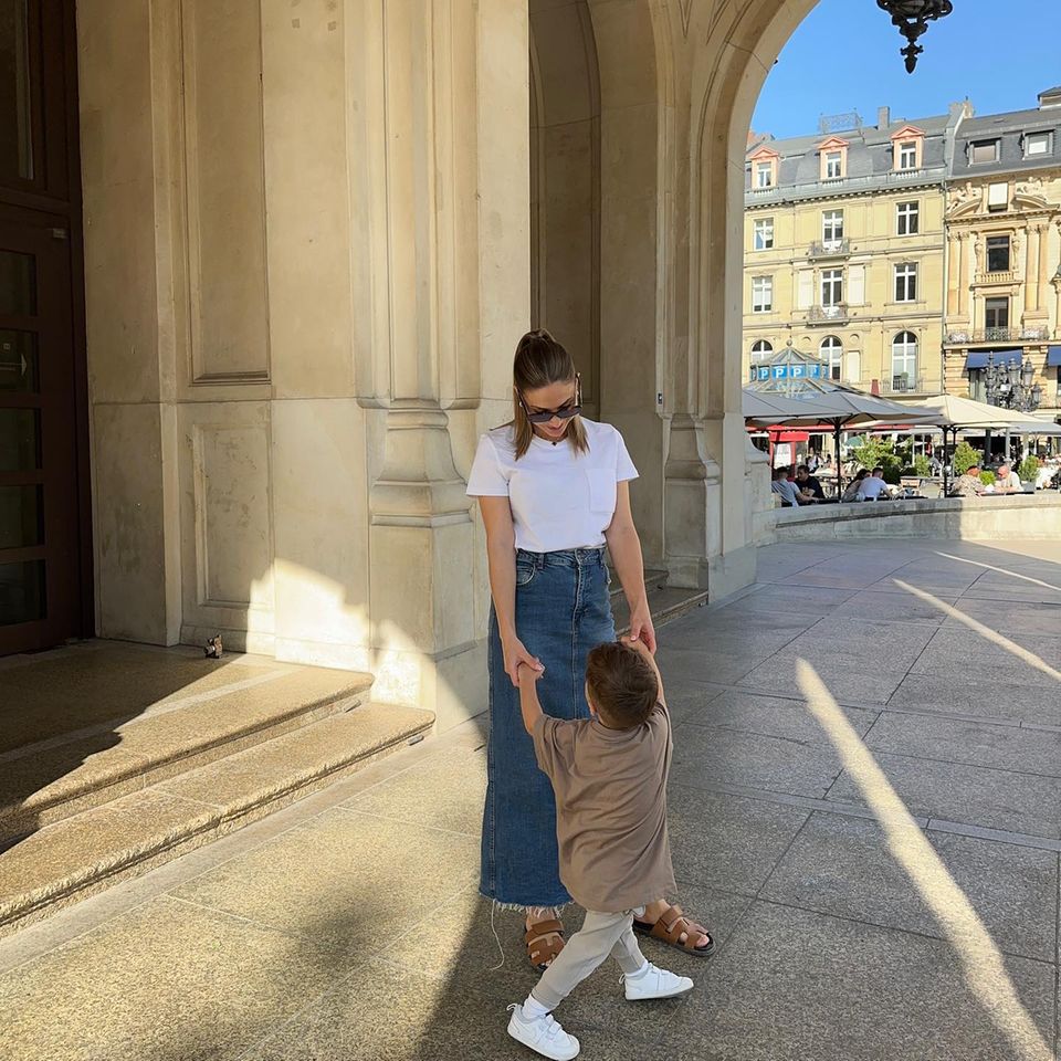 Ann-Kathrin Götze ist mit ihrem Sohn Rome unterwegs und trägt dabei DEN Sommertrend des Jahres: einen Maxi-Jeansrock. Ein weißes Basic-Shirt und Sandalen von Hèrmes vervollständigen den City-Look. 