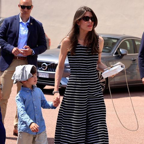 Anlässlich des 100. Geburtstags von Fürst Rainier III. (†2005) enthüllt die monegassische Fürstenfamilie neue Skulpturen in Monaco. Charlotte Casiraghi erscheint in einem schulterfreien Jumpsuit mit dünnen Querstreifen von Chanel. An der einen Hand hält sie Sohn Balthazar, in der anderen eine weiße Chanel-Tasche. 