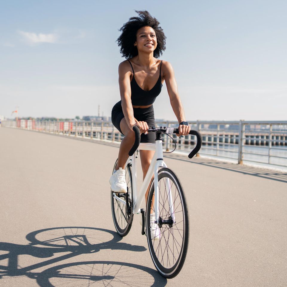 Frau fährt Fahrrad am Meer: Diese 3 Sommer-Workouts verbrennen die meisten Kalorien