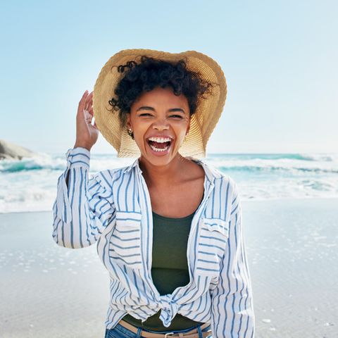 Lachende Frau am Strand: Diese 5 Eigenschaften teilen Menschen, die die kleinen Dinge des Lebens genießen