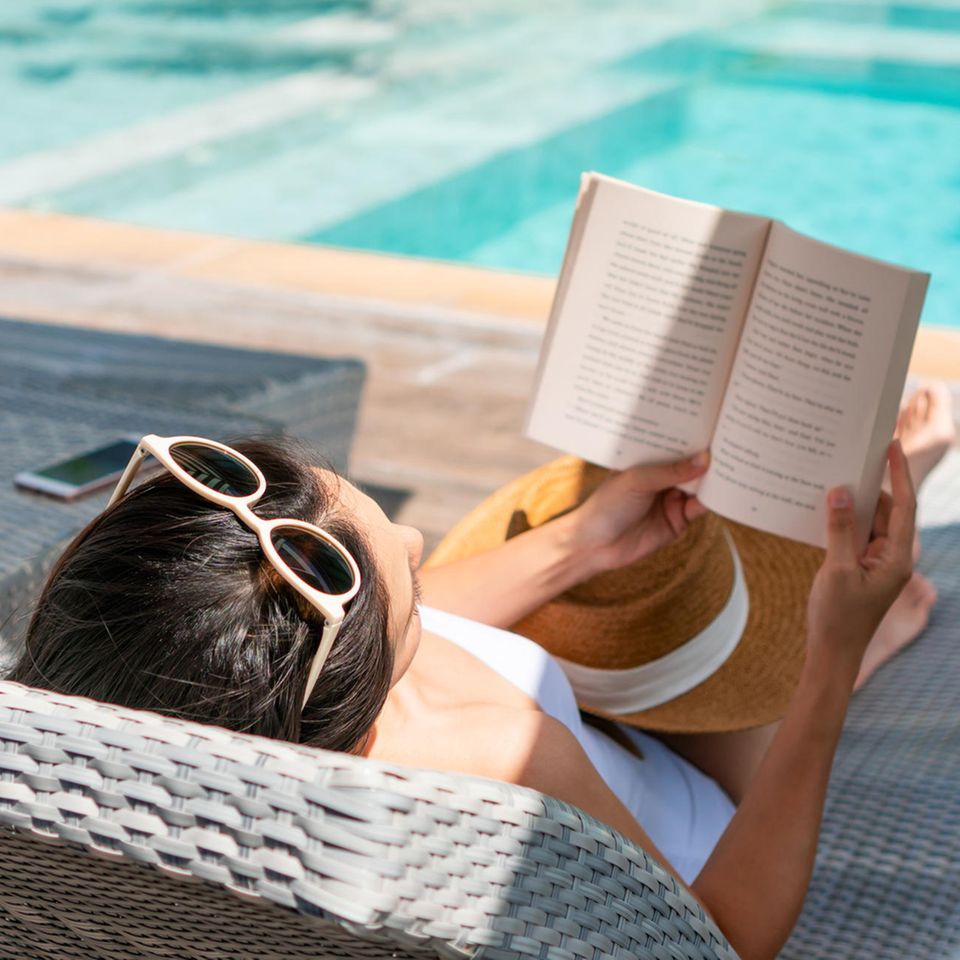 Eine Frau liest am Pool ein Buch