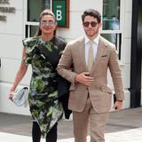 Während sich Nick Jonas für einen klassischen Anzug in Creme entscheidet, wählt seine Frau Priyanka Chopra die exzentrischere Variante. Sie erscheint in einem schwarzen Kleid mit einem blau-grünen Fleckmuster, Volants und asymmetrischem Schnitt. Overknee-Stiefel mit Peptoe-Details sowie eine schmale Sonnenbrille setzen dem Look das i-Tüpfelchen auf. 