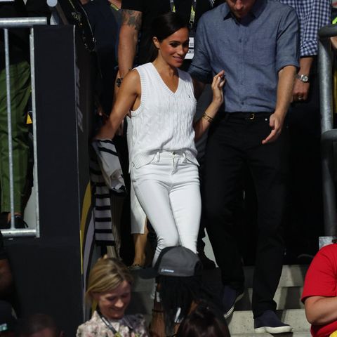Im Herzen ist sie einfach immer noch ein All-American-Girl: Die Herzogin von Sussex knüpft an ihre Style-Vorlieben vor ihrer Zeit als Senior Royal an und wählt für ein Volleyballmatch ein lässiges Ensemble. Sie setzt fast vollständig auf den All-White-Look. Zur weißen Frame-Jeans kombiniert sie einen ebenfalls weißen Strickpullunder von Polo Ralph Lauren und sorgt mit schwarzen Ballerinas von Aquazzura für Kontrast. Über dem Arm bewahrt sich die Duchess einen gestreiften Strickpullover für kühlere Stunden am Abend in Düsseldorf.  