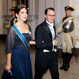 Prinzessin Mary und Prinzessin Victorias Mann Prinz Daniel kommen gemeinsam zum Jubiläumsbankett. Die dänische Prinzessin wählt für den Anlass eine dunkelblaue Robe mit transparenten Glitzerärmeln.