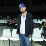 Mit blauer Kappe, übergroßer Anzugjacke, Hose und lässigem Hemd zeigt sich Cole Sprouse vor noch leeren Plätzen. 