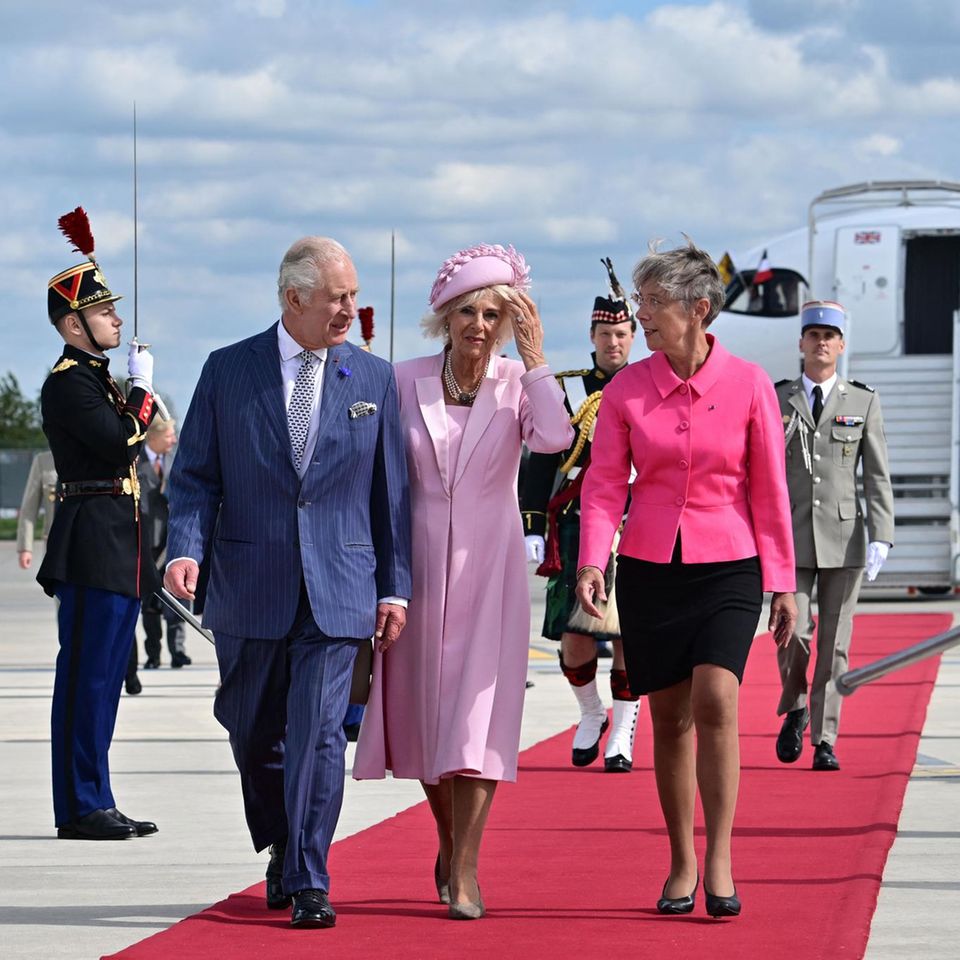 Die französische Premierministerin Elisabeth Borne nimmt König Charles und Königin Camilla am Flughafen in Empfang. Im Hintergrund ist Major Johnny Thompson zu sehen.