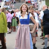 Schauspielerin Ursular Karven zeigt sich auf dem großen Volksfest der Welt in klassischer Tracht. Zum blauen Dirndl mit Schürze im verschnörkelten Streifenmuster kombiniert sie beige Wildlederboots. Kleine Blumen in den geflochtenen Zöpfen sorgen für einen spielerischen Kontrast. 