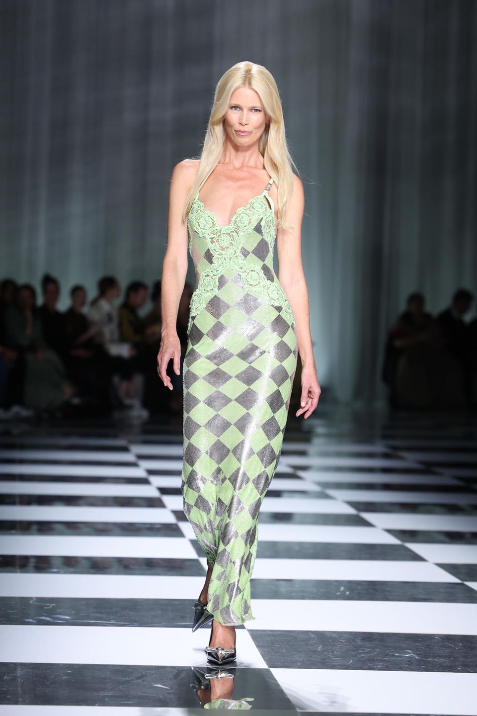Das Beste kommt zum Schluss – zumindest bei Versace. "Cloodia" ist zurück auf dem Catwalk. Für die Frrühjahr/Sommershow 2024 von Versace wird Claudia Schiffer zum Comeback auf den Laufsteg gebeten und präsentiert das finale Kleid des italienischen Modehauses. In einem grün-silbernen Kleid schwebt das 90s-Supermodel über den Runway und wird von Fans gefeiert.