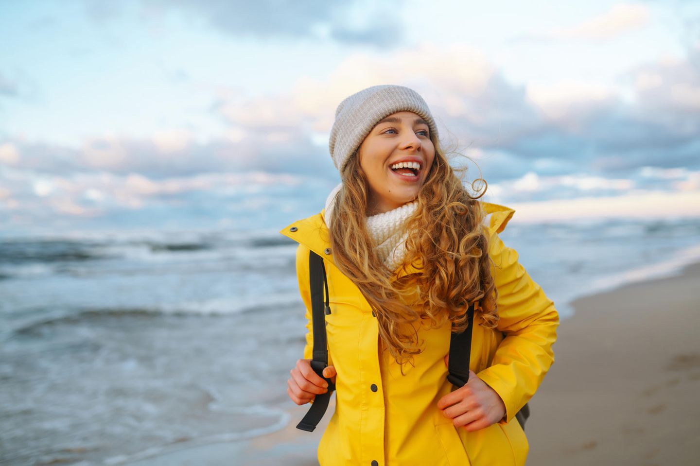 Deal des Tages: Herbstangebote für Wind und Wetter, Frau mit Regenjacke und Mütze am Strand