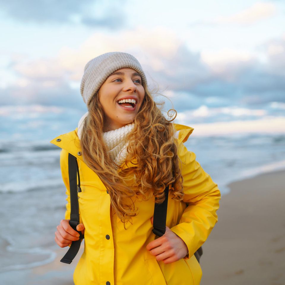 Deal des Tages: Herbstangebote für Wind und Wetter, Frau mit Regenjacke und Mütze am Strand