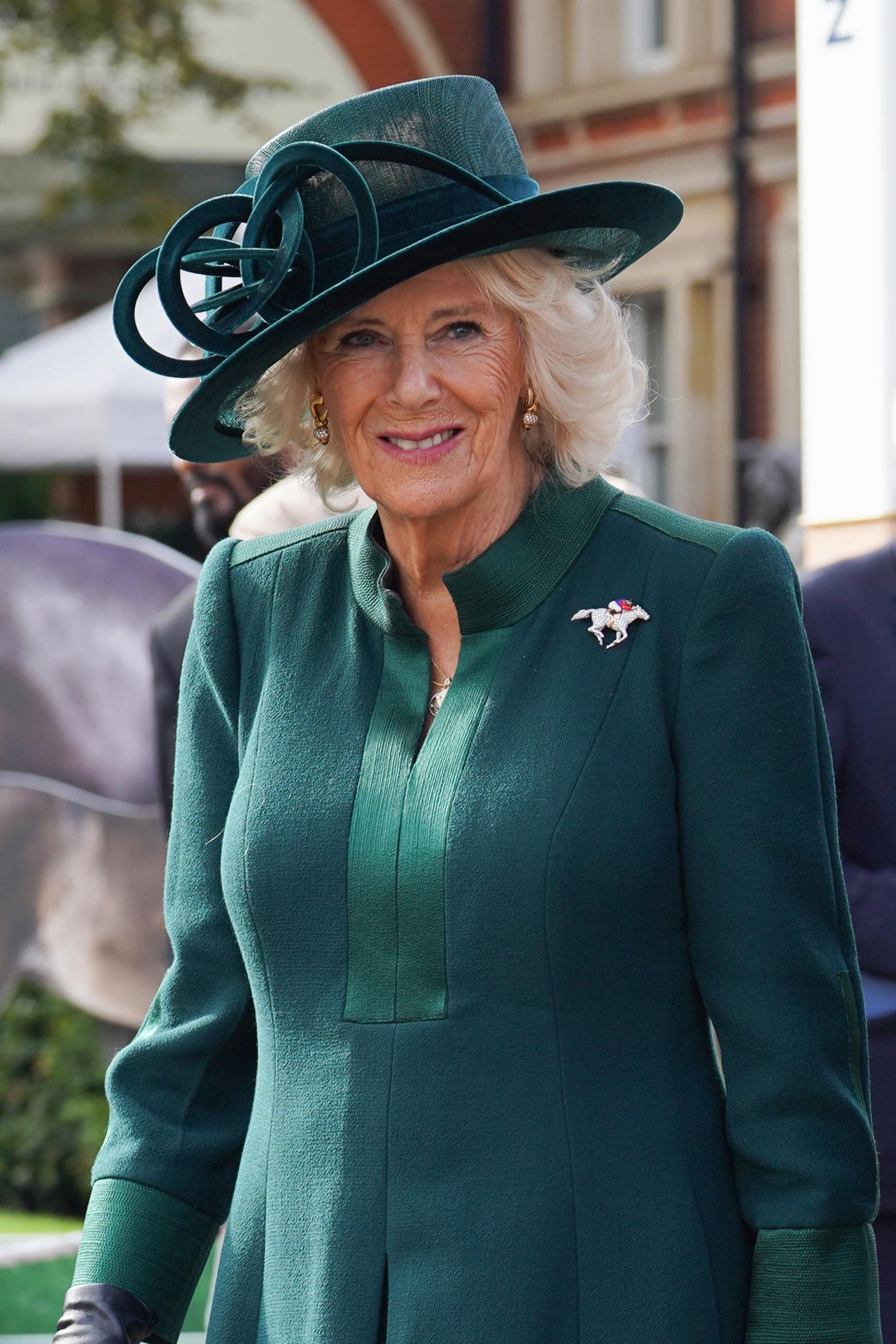 Königin Camilla zeigt sich beim British Champions Day 2023 in Ascot in anmutigem Petrolgrün. Doch die elegante Farbe ist nicht der eigentliche Hingucker ihres Looks, sondern das Augenmerk liegt auf der ausgefallenen Brosche. Diese zeigt ein mit Diamanten besetztes Pferd, welches von einem Rennreiter geritten wird. Die hochwertige Brosche wurde einst Königin Elizabeth II. zu ihrem 90. Geburtstag geschenkt, nach ihrem Tod ging das Schmuckstück an Königin Camilla, die sich genauso für diesen Sport begeistern kann. Dass Camilla nun also dieses Schmuckstück trägt, ist eine schöne Geste in Erinnerung an ihre Schwiegermutter. 