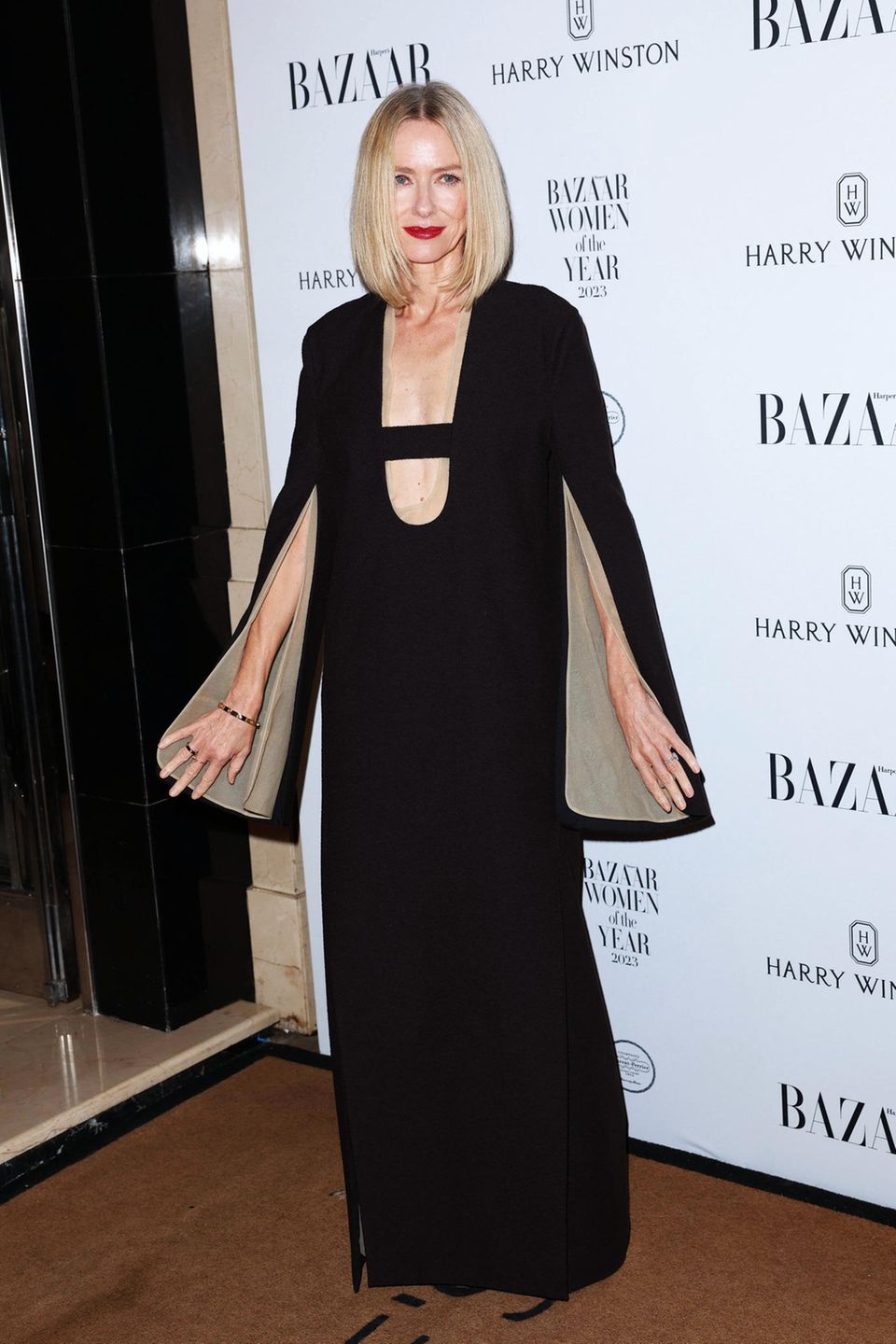 Eleganz trifft Extravaganz: Naomi Watts präsentiert sich in London im schwarzen, bodenlangen Kleid von Tory Burch. Hingucker sind die offenen Ärmel und der tiefe Steg-Ausschnitt.
