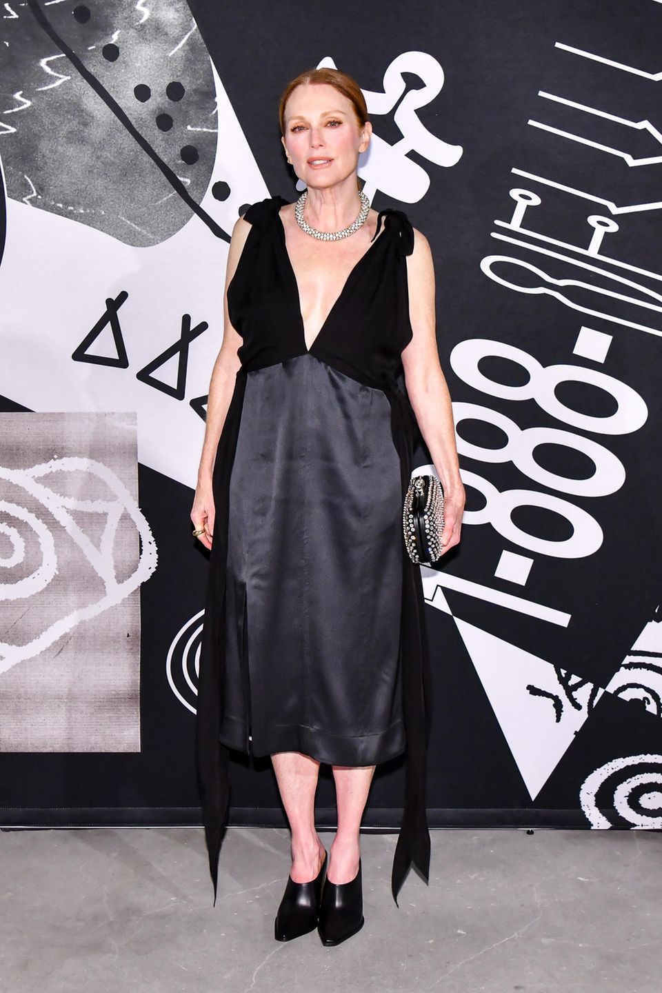 In einem tiefausgeschnittenen Kleid mit Schleifendetails an den Schultern von Bottega Veneta nimmt auch Julianne Moore an dem Event teil. Eine Clutch mit Strasssteinen, silberner Schmuck und Mules vervollständigen den Look der Oscar-Preisträgerin.